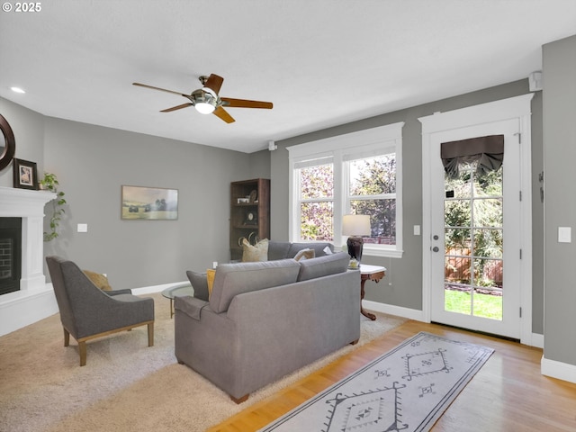 living room featuring baseboards, a ceiling fan, light wood finished floors, and a glass covered fireplace