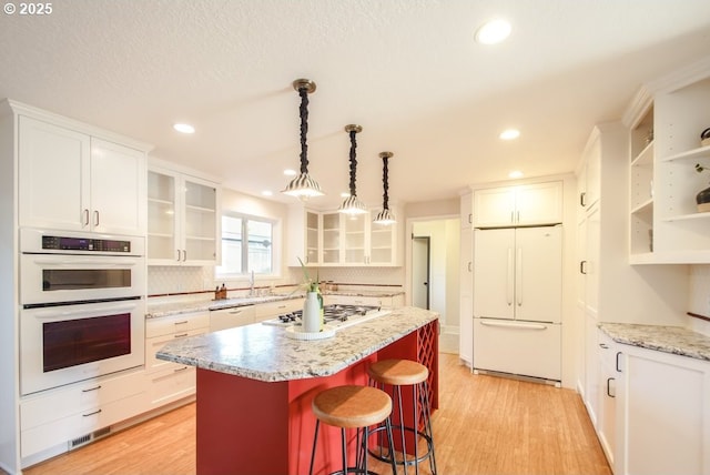 2440 SW Burbank Ave, Portland, OR 97225 - kitchen with white appliances, white cabinetry, light wood finished floors, a center island, and tasteful backsplash