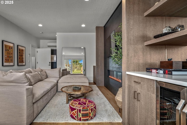 living area featuring beverage cooler, a wall mounted AC, recessed lighting, a fireplace, and light wood finished floors