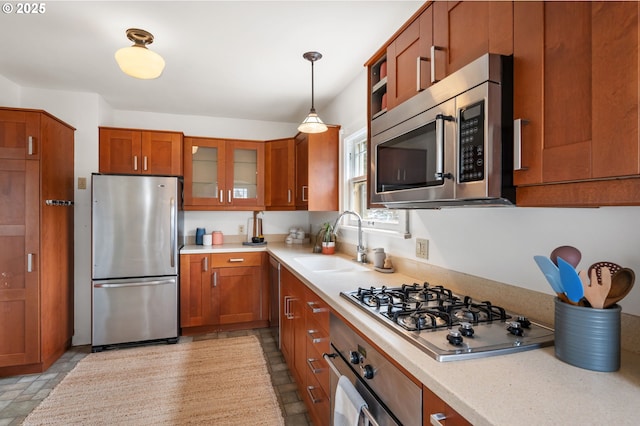 kitchen with a sink, stainless steel appliances, brown cabinetry, light countertops, and glass insert cabinets