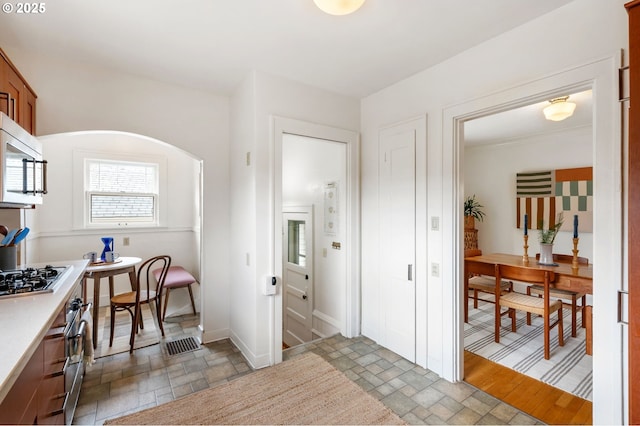 interior space featuring arched walkways, visible vents, baseboards, and stone tile flooring