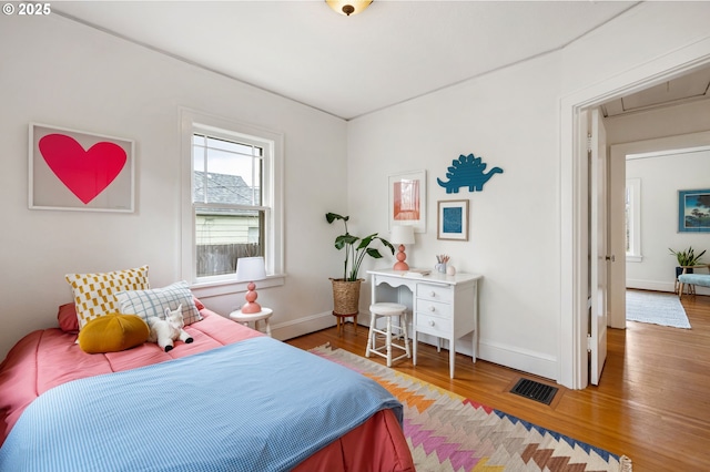 bedroom featuring visible vents, attic access, baseboards, and wood finished floors