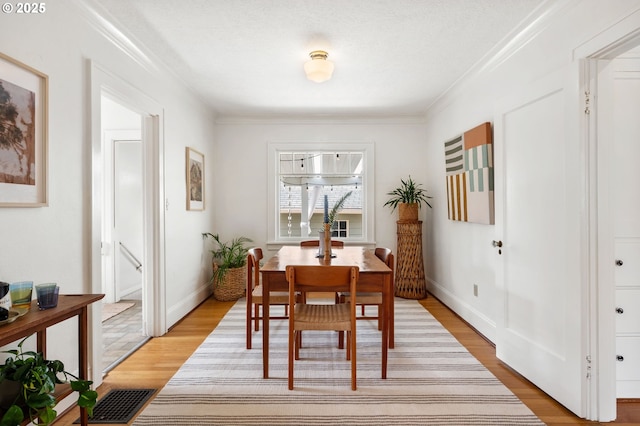 dining area featuring crown molding, visible vents, light wood-type flooring, and baseboards