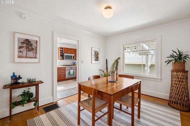 dining area featuring crown molding, baseboards, visible vents, and light wood finished floors