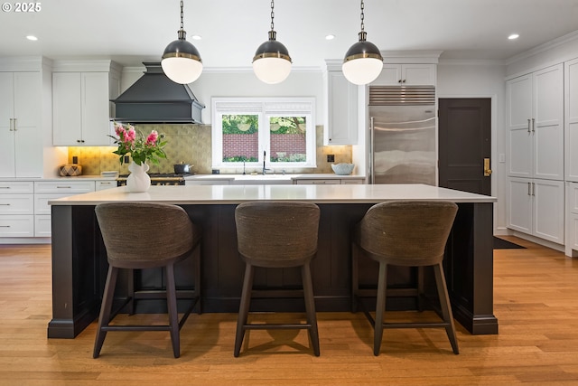 kitchen featuring built in fridge, custom range hood, a sink, a center island, and light countertops