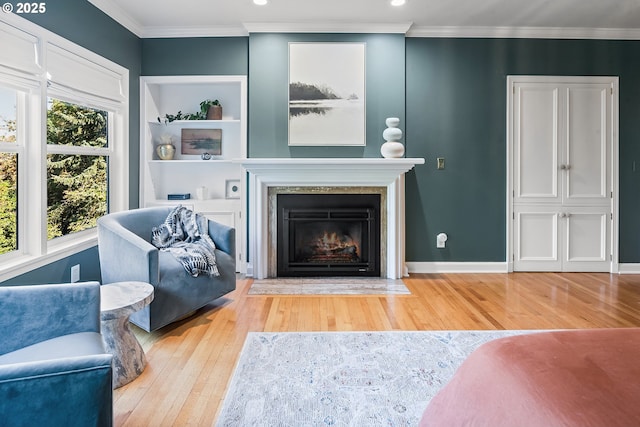 living area featuring wood finished floors, a fireplace with flush hearth, recessed lighting, ornamental molding, and baseboards
