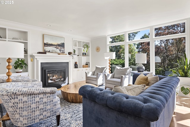 living room featuring built in shelves, a glass covered fireplace, wood finished floors, and ornamental molding