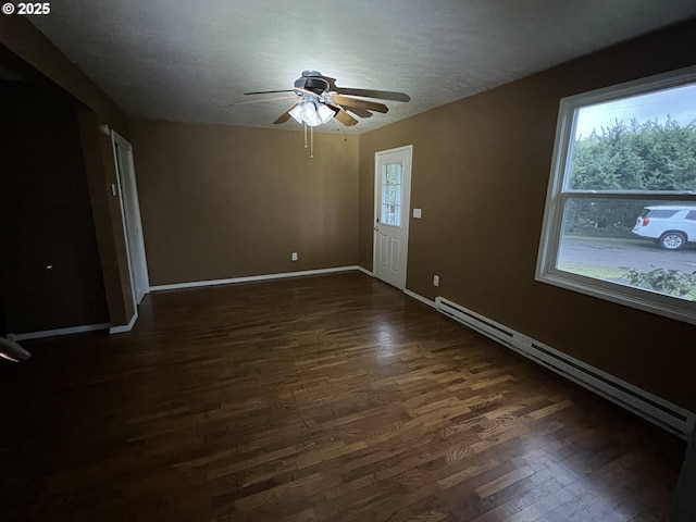 empty room featuring a baseboard heating unit, plenty of natural light, and dark hardwood / wood-style floors