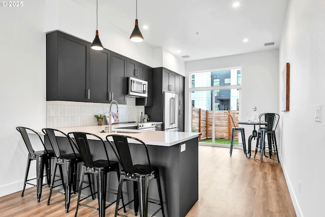 kitchen with kitchen peninsula, appliances with stainless steel finishes, backsplash, a breakfast bar, and hanging light fixtures