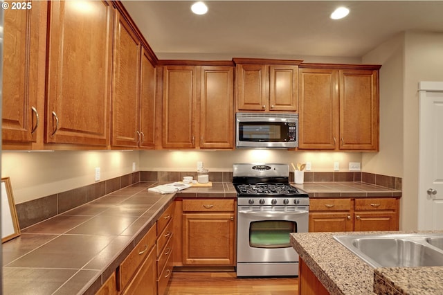 kitchen with sink, tile counters, stainless steel appliances, and light hardwood / wood-style floors