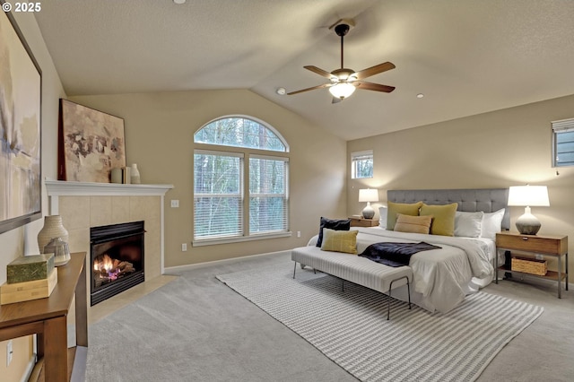 carpeted bedroom featuring ceiling fan, vaulted ceiling, a tile fireplace, and a textured ceiling