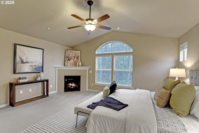 carpeted bedroom with a tiled fireplace, lofted ceiling, and ceiling fan