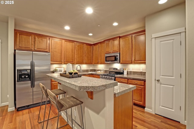 kitchen with sink, light hardwood / wood-style flooring, appliances with stainless steel finishes, a kitchen breakfast bar, and a kitchen island