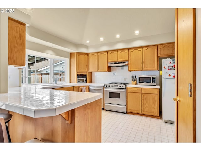 kitchen featuring tile counters, stainless steel appliances, a peninsula, decorative backsplash, and range hood