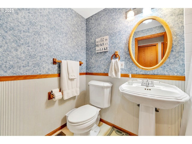 half bath featuring toilet, wallpapered walls, and a sink
