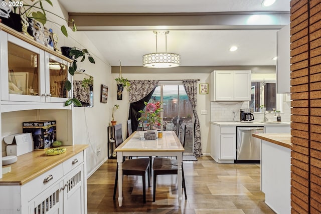 kitchen featuring decorative backsplash, dishwasher, butcher block countertops, white cabinetry, and a sink