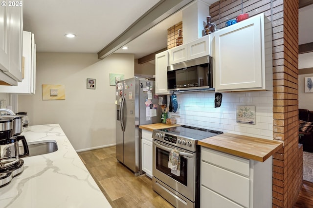 kitchen featuring stainless steel appliances, white cabinets, butcher block countertops, and tasteful backsplash