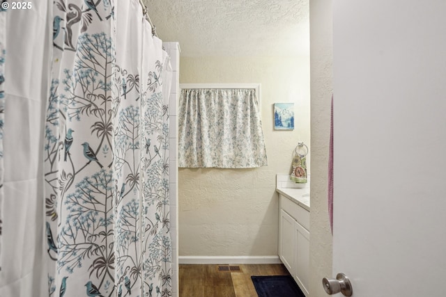 full bath featuring curtained shower, a textured wall, a textured ceiling, wood finished floors, and baseboards