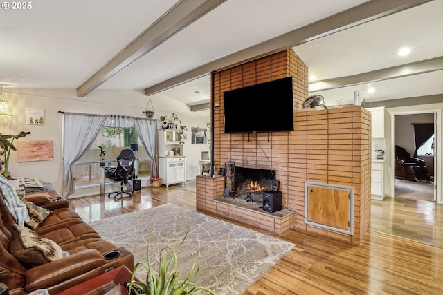 living area with a brick fireplace, beam ceiling, and wood finished floors