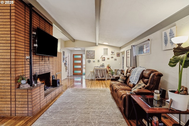 living room featuring plenty of natural light, lofted ceiling with beams, a brick fireplace, and wood finished floors