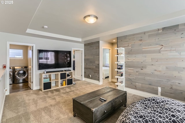 carpeted living room featuring baseboards, wood walls, and independent washer and dryer