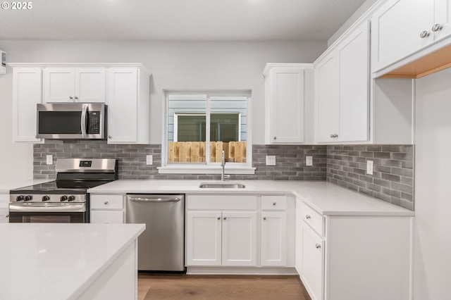 kitchen featuring stainless steel appliances, a sink, white cabinets, light countertops, and tasteful backsplash