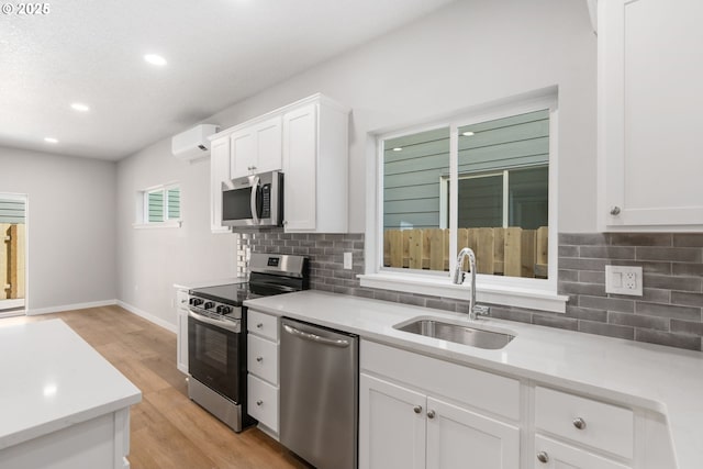 kitchen with light wood finished floors, white cabinets, appliances with stainless steel finishes, a sink, and a wall mounted AC