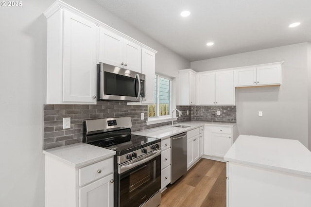 kitchen featuring stainless steel appliances, tasteful backsplash, light wood-style floors, white cabinetry, and a sink