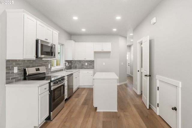 kitchen featuring light wood finished floors, decorative backsplash, appliances with stainless steel finishes, white cabinets, and a sink