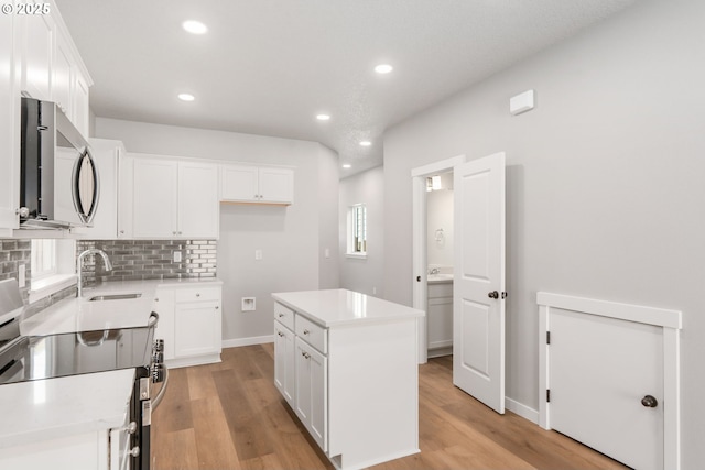 kitchen with white cabinets, decorative backsplash, stainless steel appliances, light wood-type flooring, and a sink