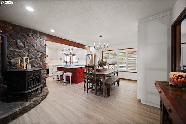 dining room featuring a textured ceiling, a chandelier, light wood-type flooring, and a wood stove