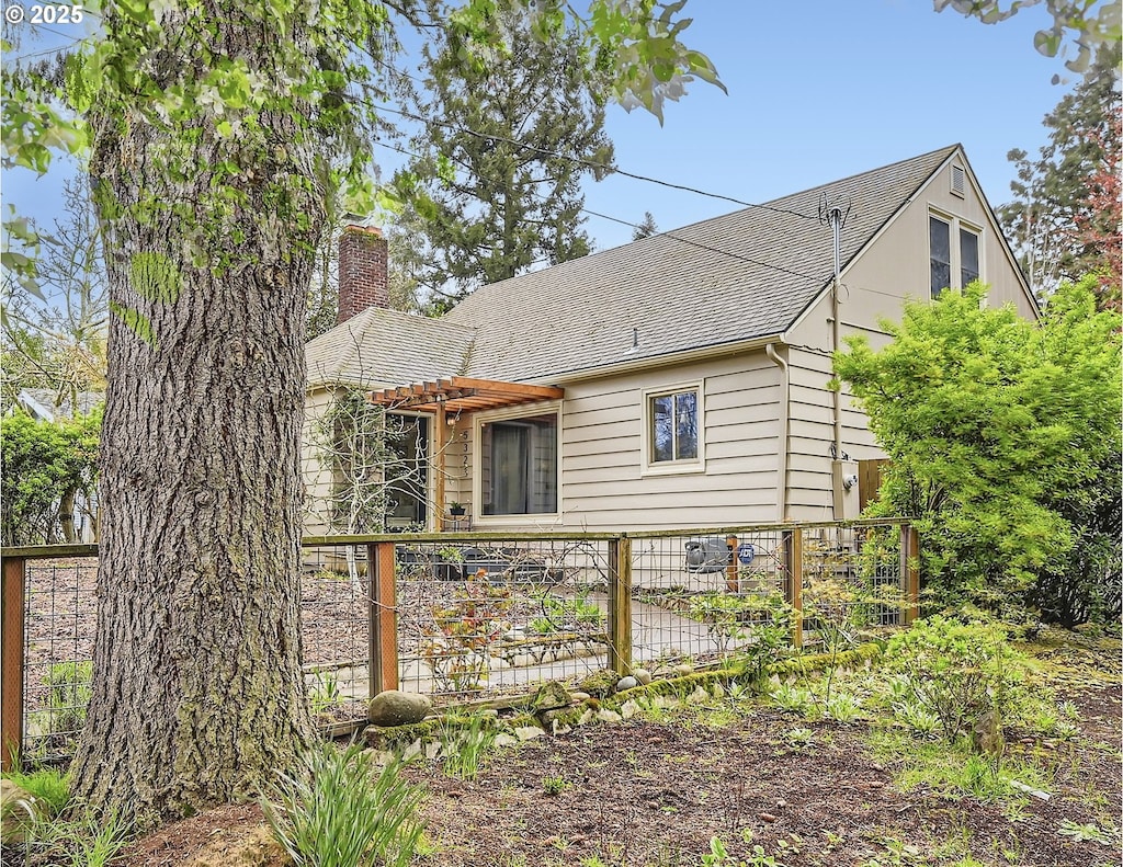 rear view of house featuring a pergola, roof with shingles, fence, and a chimney