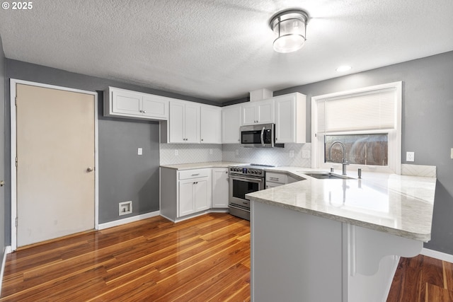 kitchen with sink, appliances with stainless steel finishes, white cabinetry, hardwood / wood-style floors, and kitchen peninsula