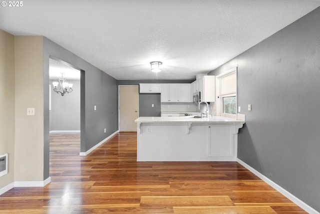 kitchen featuring a kitchen bar, sink, white cabinetry, wood-type flooring, and kitchen peninsula