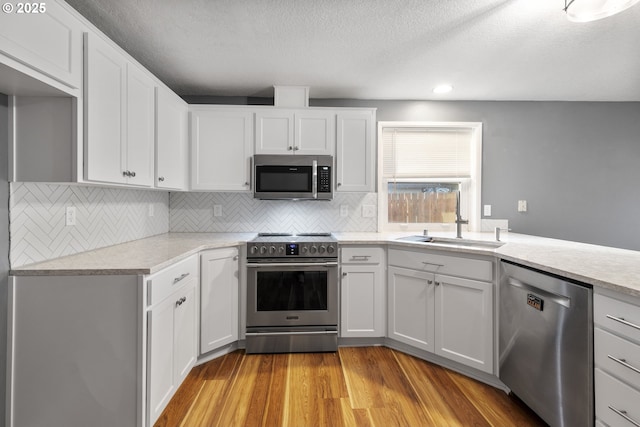 kitchen featuring sink, appliances with stainless steel finishes, light hardwood / wood-style floors, white cabinets, and decorative backsplash