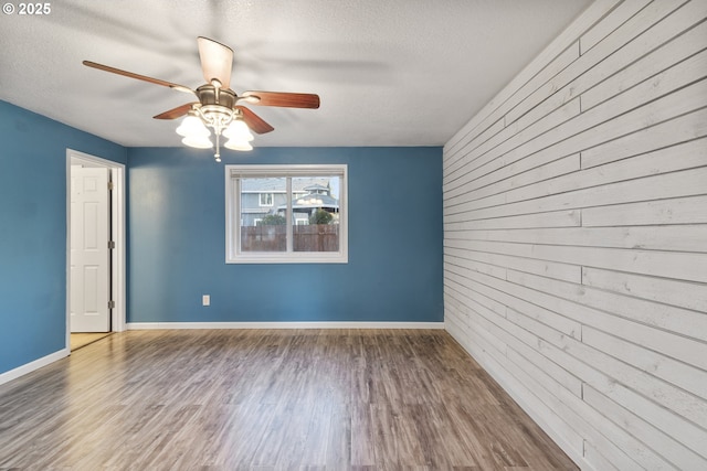 unfurnished room with ceiling fan, hardwood / wood-style floors, a textured ceiling, and wood walls