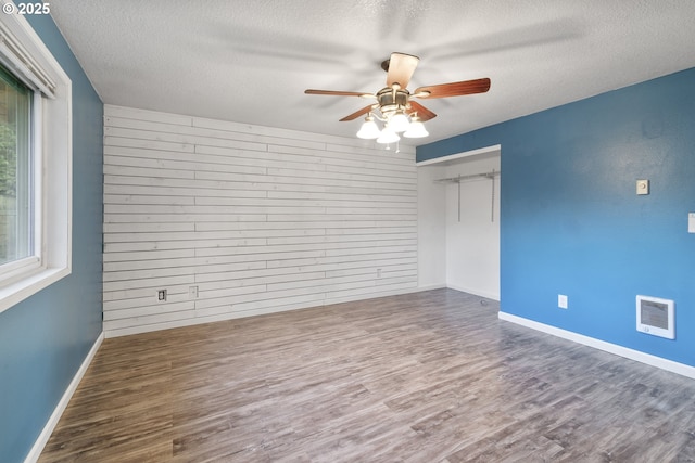 unfurnished room with ceiling fan, a textured ceiling, dark hardwood / wood-style flooring, and wood walls