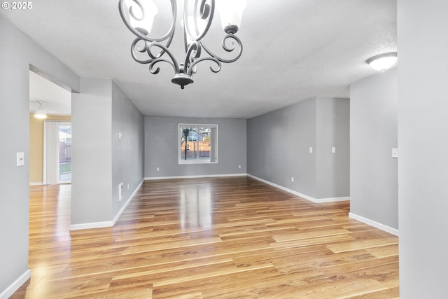 unfurnished dining area featuring a notable chandelier, a wealth of natural light, a textured ceiling, and light wood-type flooring