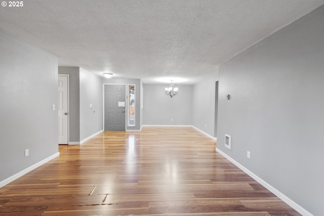 unfurnished room with wood-type flooring, a textured ceiling, and an inviting chandelier