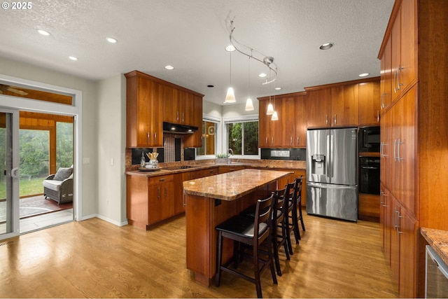22767 SW Saunders Dr, Sherwood, OR 97140 - kitchen with black appliances, brown cabinetry, under cabinet range hood, light wood-style floors, and recessed lighting