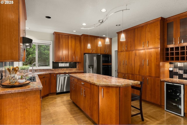 22767 SW Saunders Dr, Sherwood, OR 97140 - kitchen featuring wine cooler, black appliances, a sink, brown cabinetry, and a center island