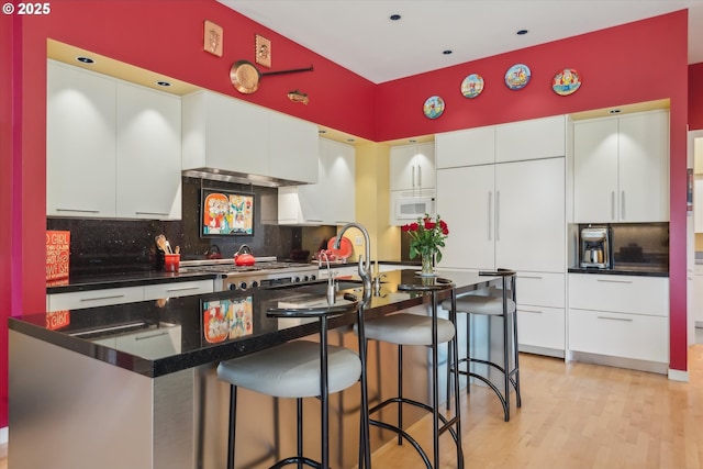 kitchen featuring white cabinetry, backsplash, white microwave, and a kitchen bar