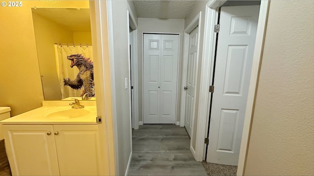 full bath featuring a textured wall, a textured ceiling, vanity, and wood finished floors