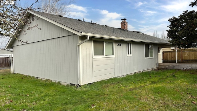 rear view of property with a yard, fence, a chimney, and a shingled roof