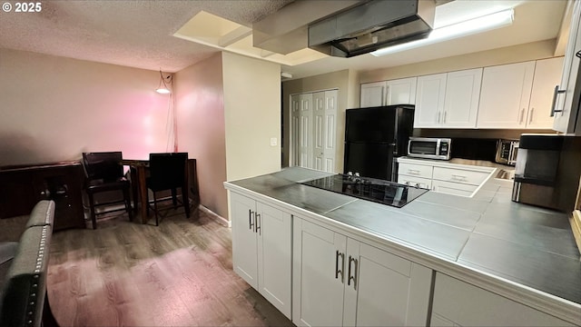 kitchen featuring a textured ceiling, white cabinetry, light wood-style floors, tile counters, and black appliances