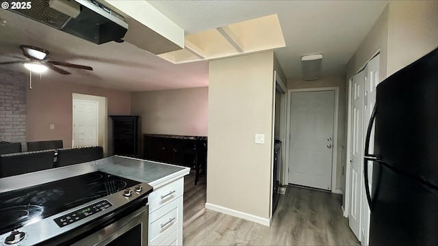 kitchen featuring light wood finished floors, baseboards, freestanding refrigerator, stainless steel range with electric cooktop, and white cabinetry