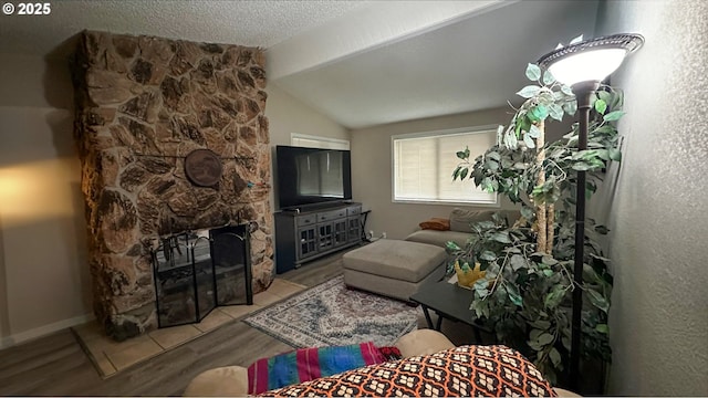 living area featuring vaulted ceiling, a fireplace, a textured ceiling, and wood finished floors