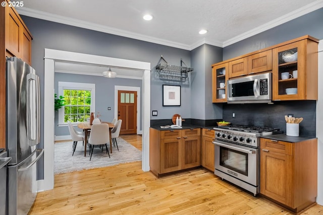 kitchen featuring stainless steel appliances, light wood-style flooring, dark countertops, ornamental molding, and glass insert cabinets
