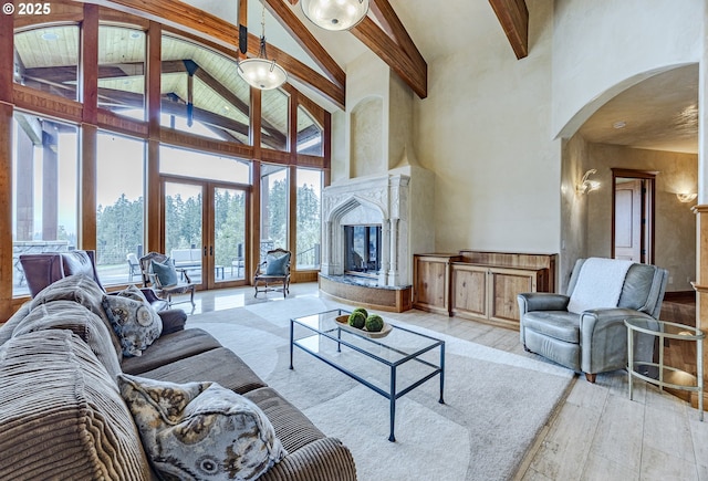 living area featuring arched walkways, french doors, beam ceiling, a premium fireplace, and light wood-style floors