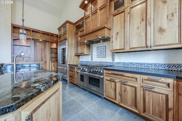 kitchen with premium appliances, pendant lighting, dark countertops, glass insert cabinets, and a sink